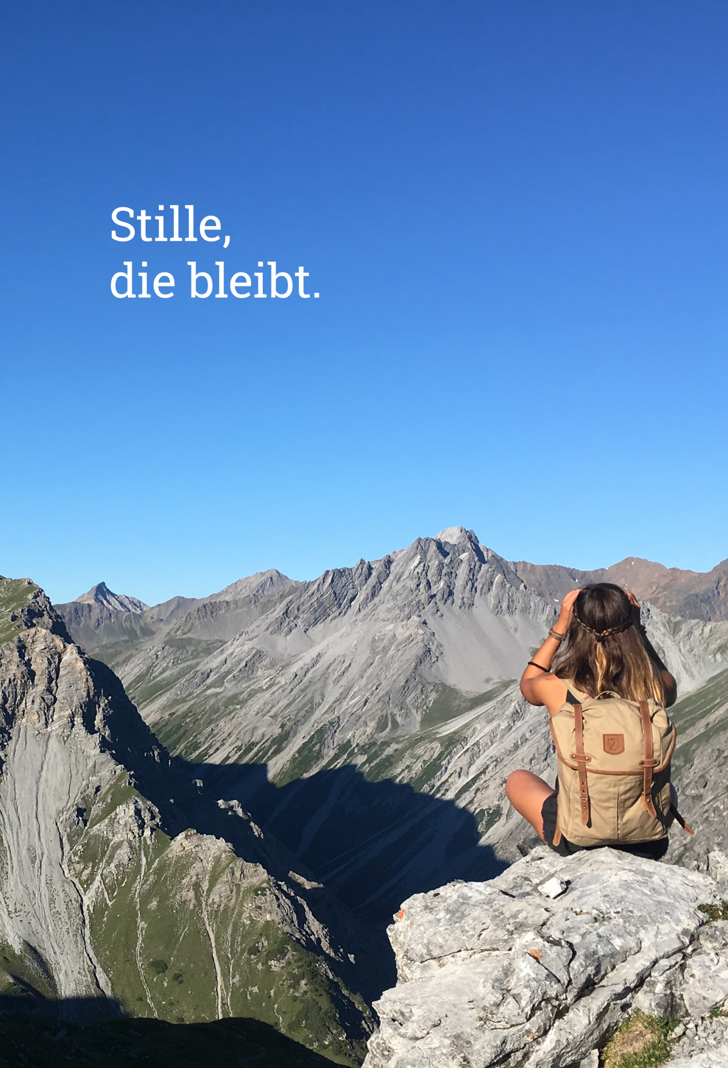 Eine Wanderin sitzt auf einem Felsvorsprung und blickt über eine weite Berglandschaft in den Alpen bei klarem Himmel.